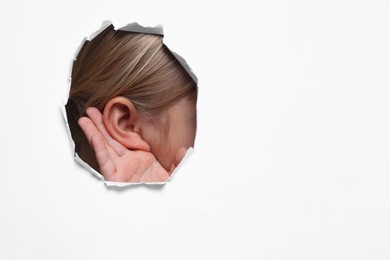 Photo of Little girl showing hand to ear gesture through hole in white paper, closeup. Space for text