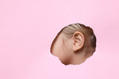 Little girl showing her ear through hole in pink paper, closeup. Space for text