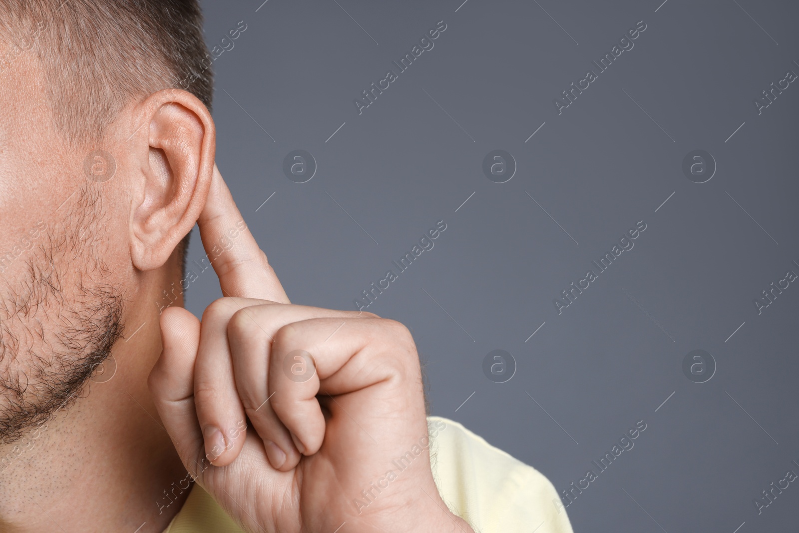 Photo of Man showing hand to ear gesture on grey background, closeup. Space for text