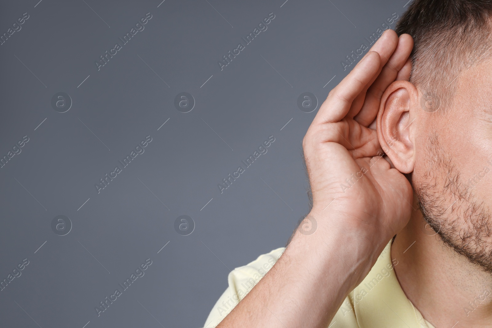 Photo of Man showing hand to ear gesture on grey background, closeup. Space for text