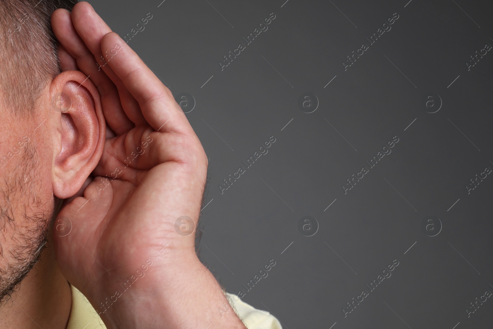 Photo of Man showing hand to ear gesture on grey background, closeup. Space for text