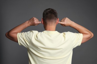 Photo of Man covering his ears with fingers on grey background, back view