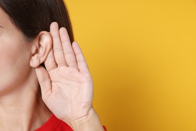 Photo of Woman showing hand to ear gesture on orange background, closeup. Space for text