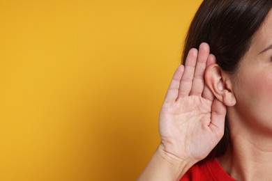 Photo of Woman showing hand to ear gesture on orange background, closeup. Space for text