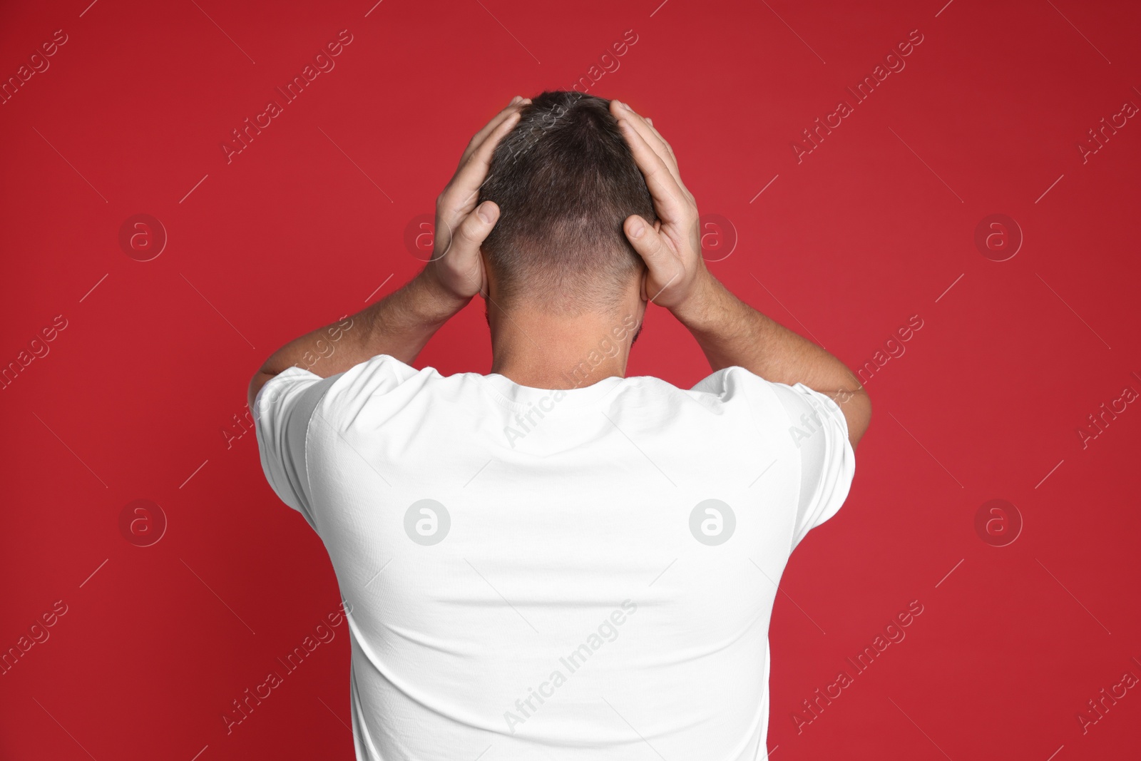 Photo of Man covering his ears on red background, back view