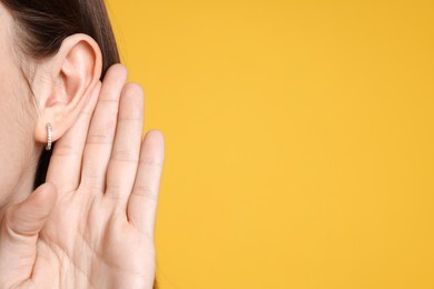 Photo of Woman showing hand to ear gesture on orange background, closeup. Space for text