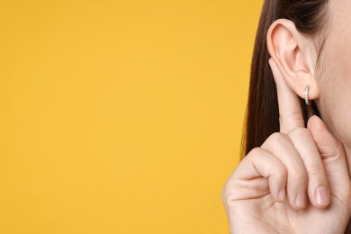 Photo of Woman showing hand to ear gesture on orange background, closeup. Space for text