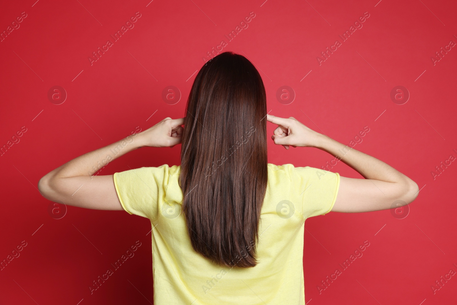 Photo of Woman covering her ears with fingers on red background, back view