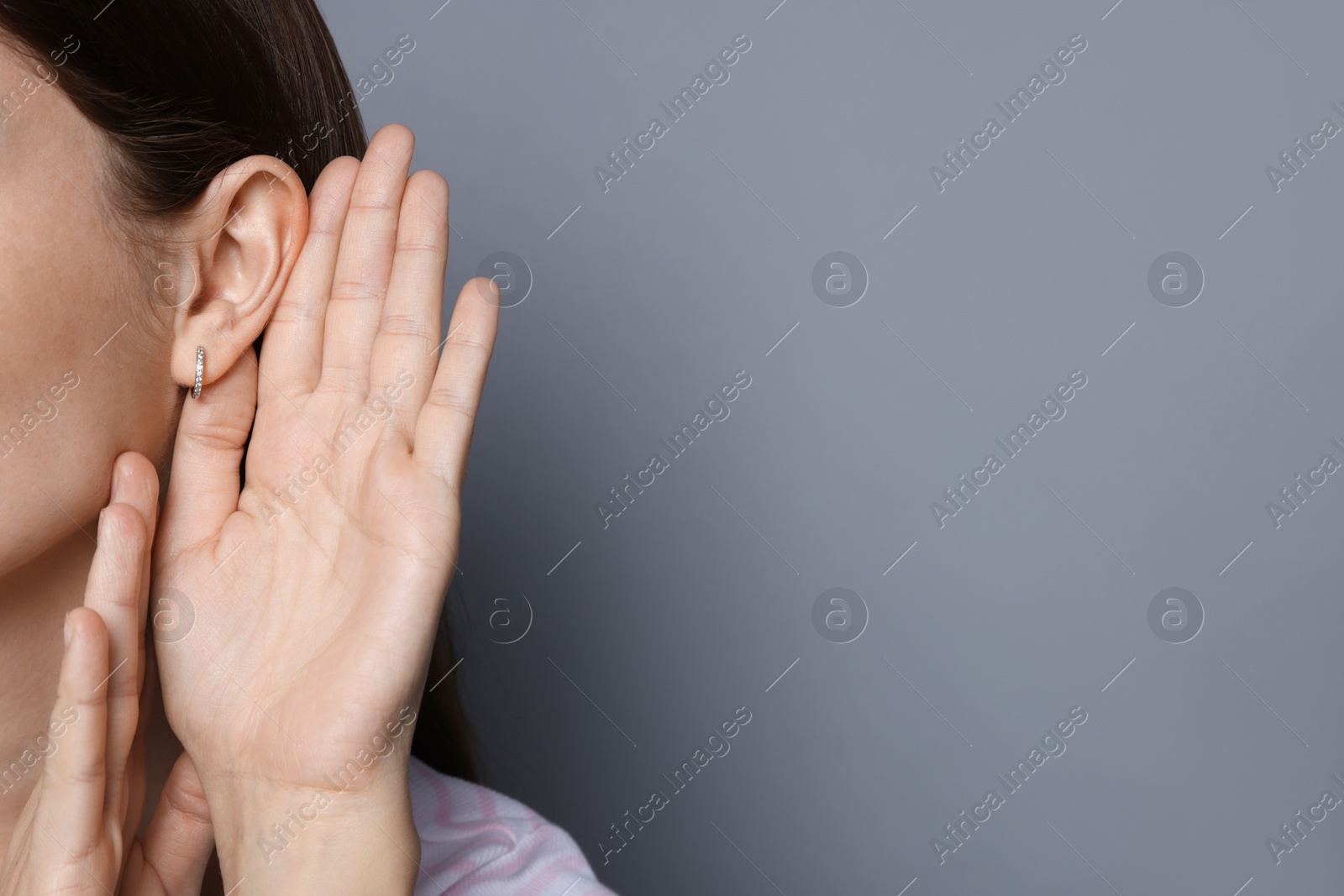 Photo of Woman showing hand to ear gesture on grey background, closeup. Space for text