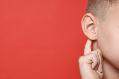 Little boy showing hand to ear gesture on red background, closeup. Space for text