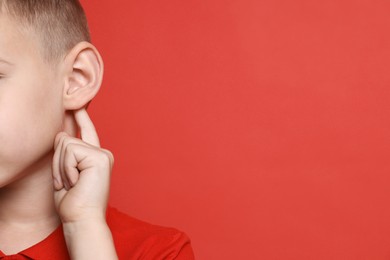 Photo of Little boy showing hand to ear gesture on red background, closeup. Space for text