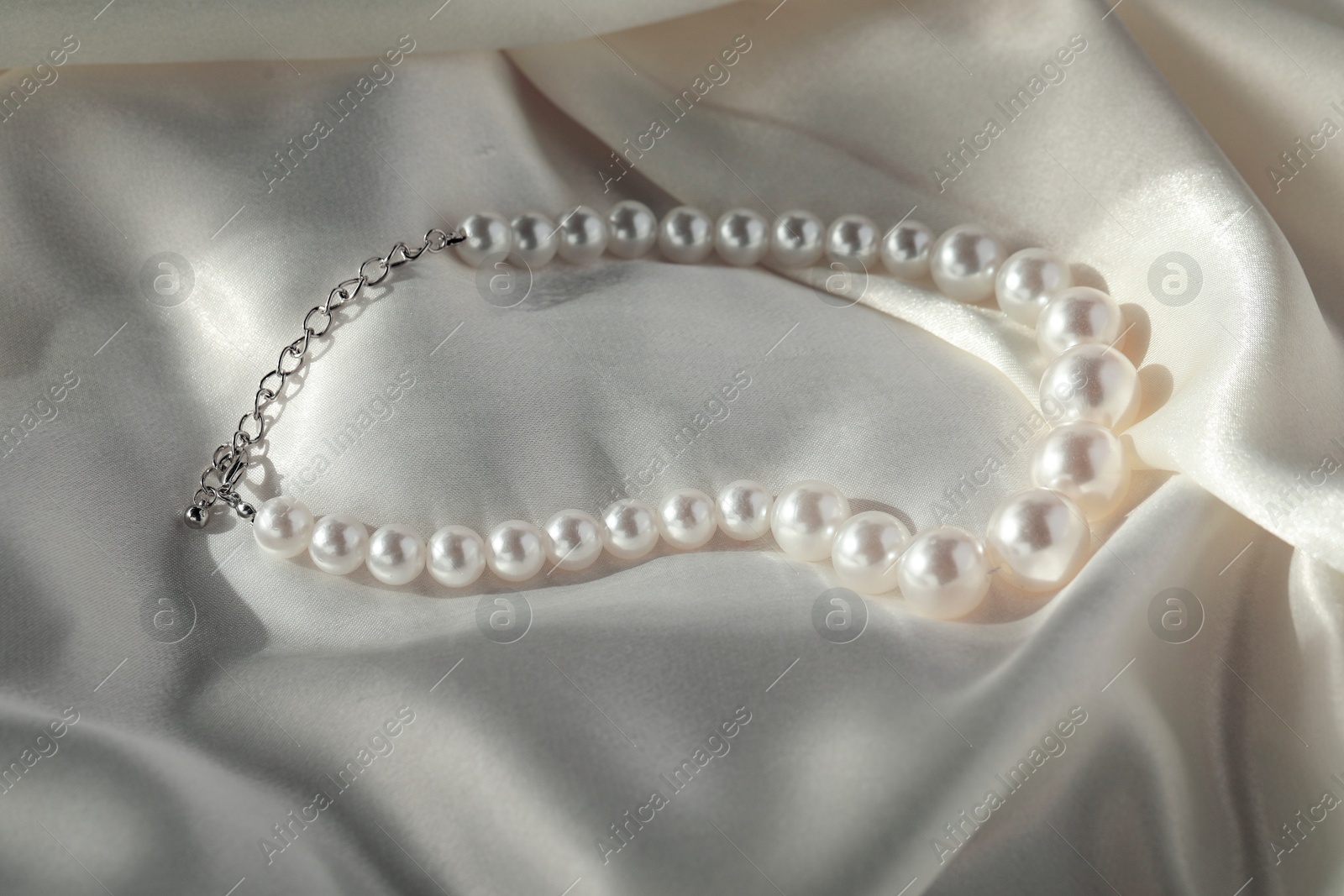 Photo of Beautiful pearl necklace on white silk, closeup