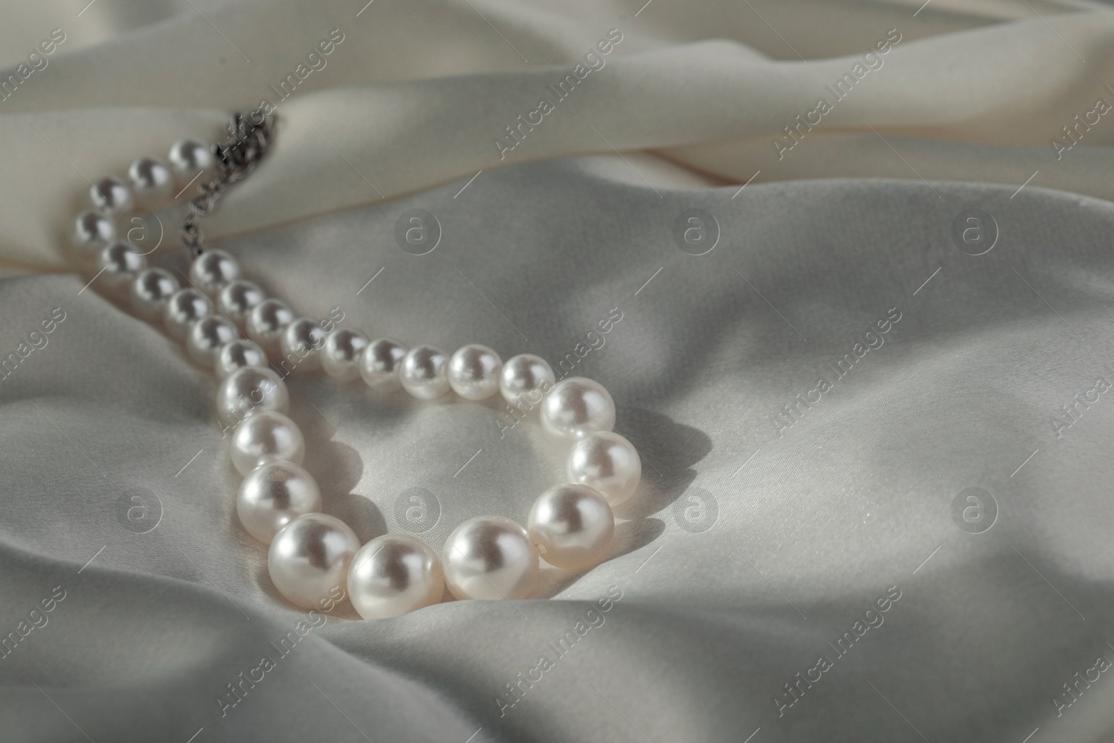 Photo of Beautiful pearl necklace on white silk, closeup. Space for text