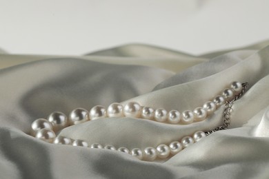 Photo of Beautiful pearl necklace on white silk, closeup