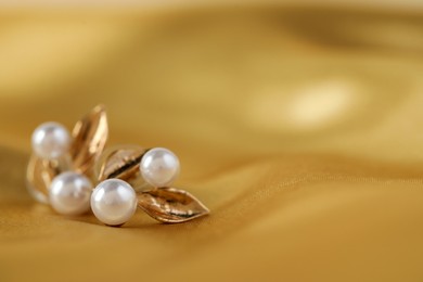 Photo of Beautiful pearl earrings on golden silk, closeup. Space for text