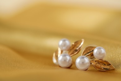 Photo of Beautiful pearl earrings on golden silk, closeup. Space for text