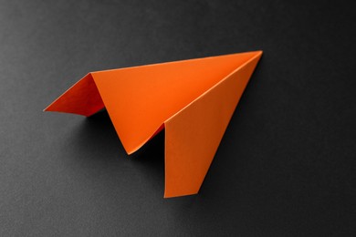 Photo of One handmade orange paper plane on black background, closeup