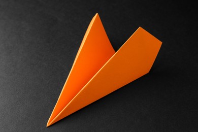 Photo of One handmade orange paper plane on black background, closeup