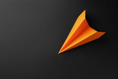 Photo of One handmade orange paper plane on black background, top view. Space for text