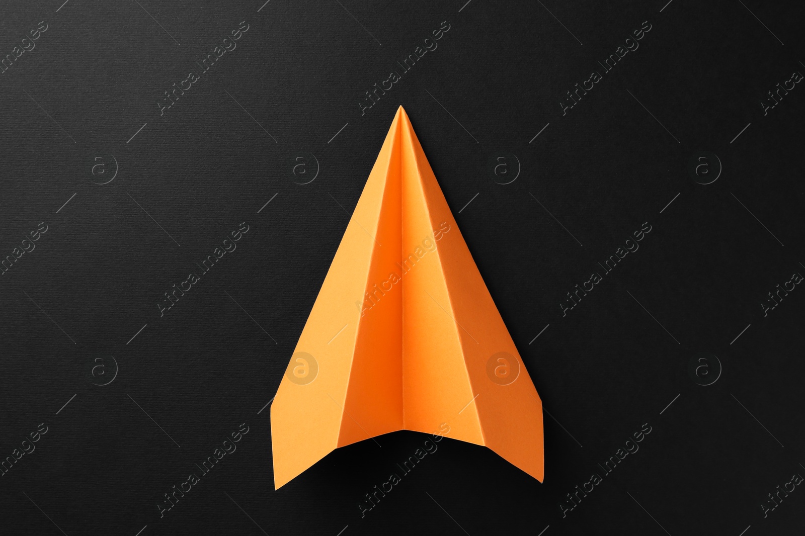 Photo of One handmade orange paper plane on black background, top view