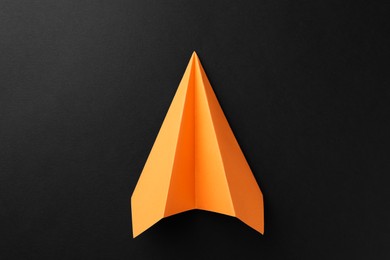 Photo of One handmade orange paper plane on black background, top view