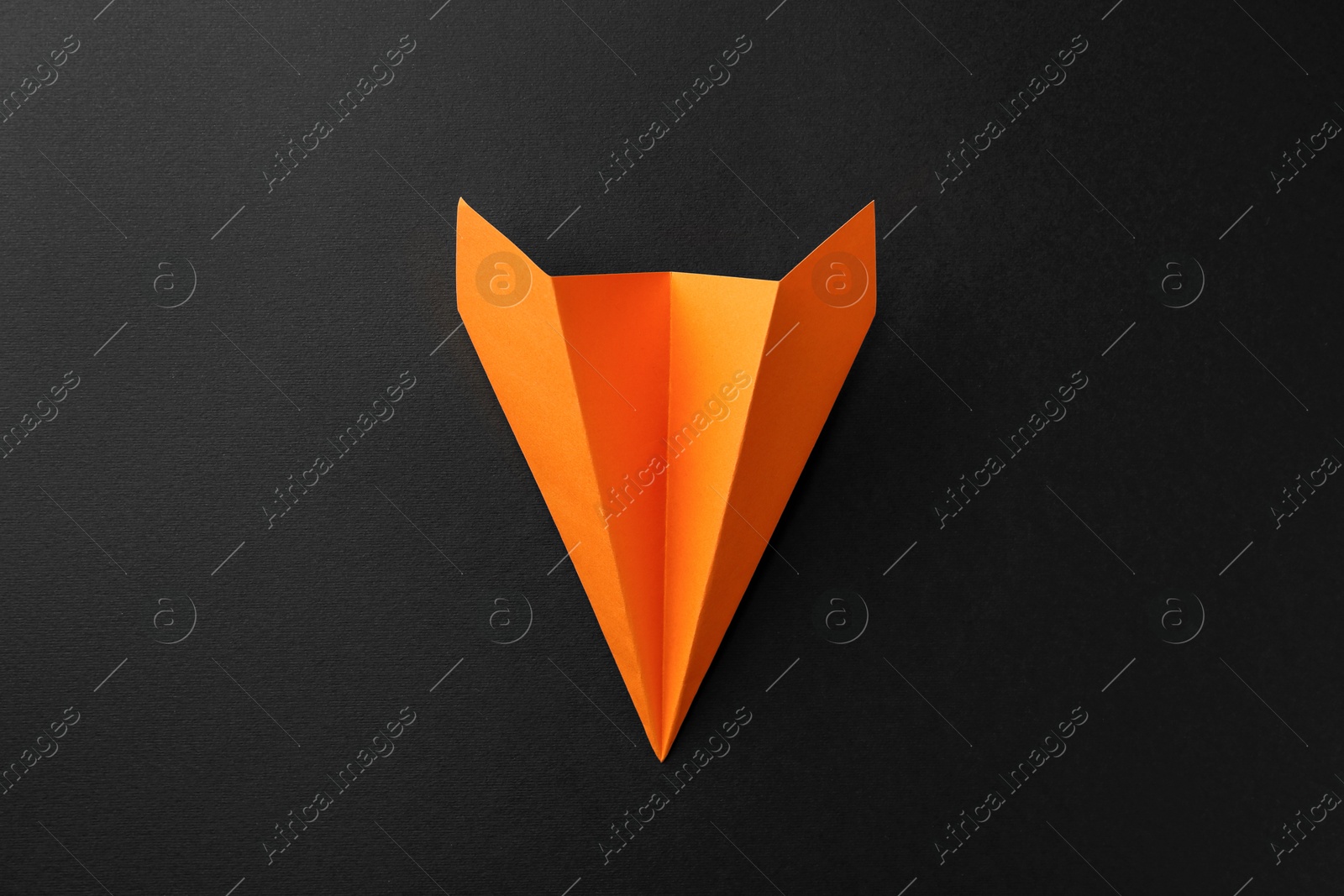 Photo of One handmade orange paper plane on black background, top view