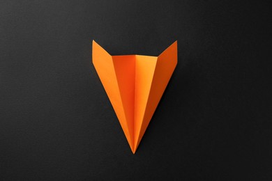 Photo of One handmade orange paper plane on black background, top view