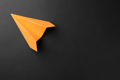 Photo of One handmade orange paper plane on black background, top view. Space for text