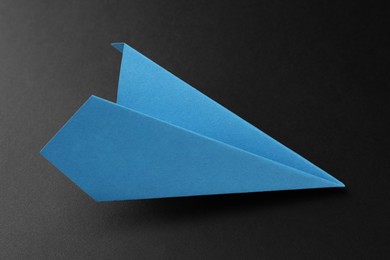 Photo of One handmade light blue paper plane on black background, closeup