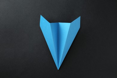 Photo of One handmade light blue paper plane on black background, top view