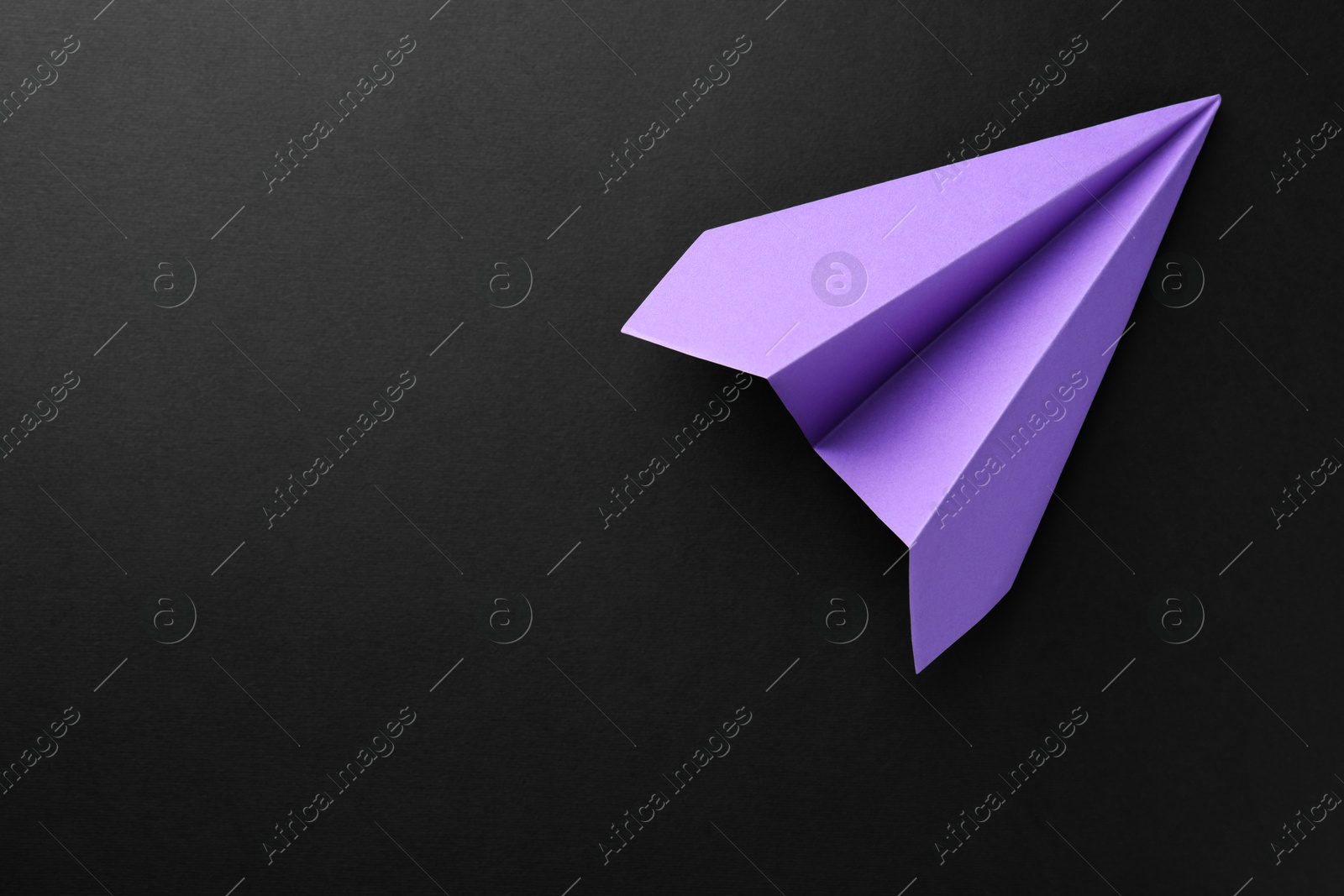 Photo of One handmade violet paper plane on black background, top view. Space for text