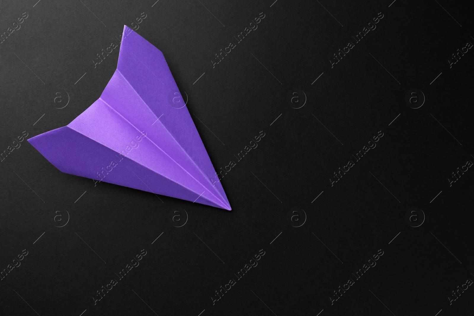 Photo of One handmade violet paper plane on black background, top view. Space for text