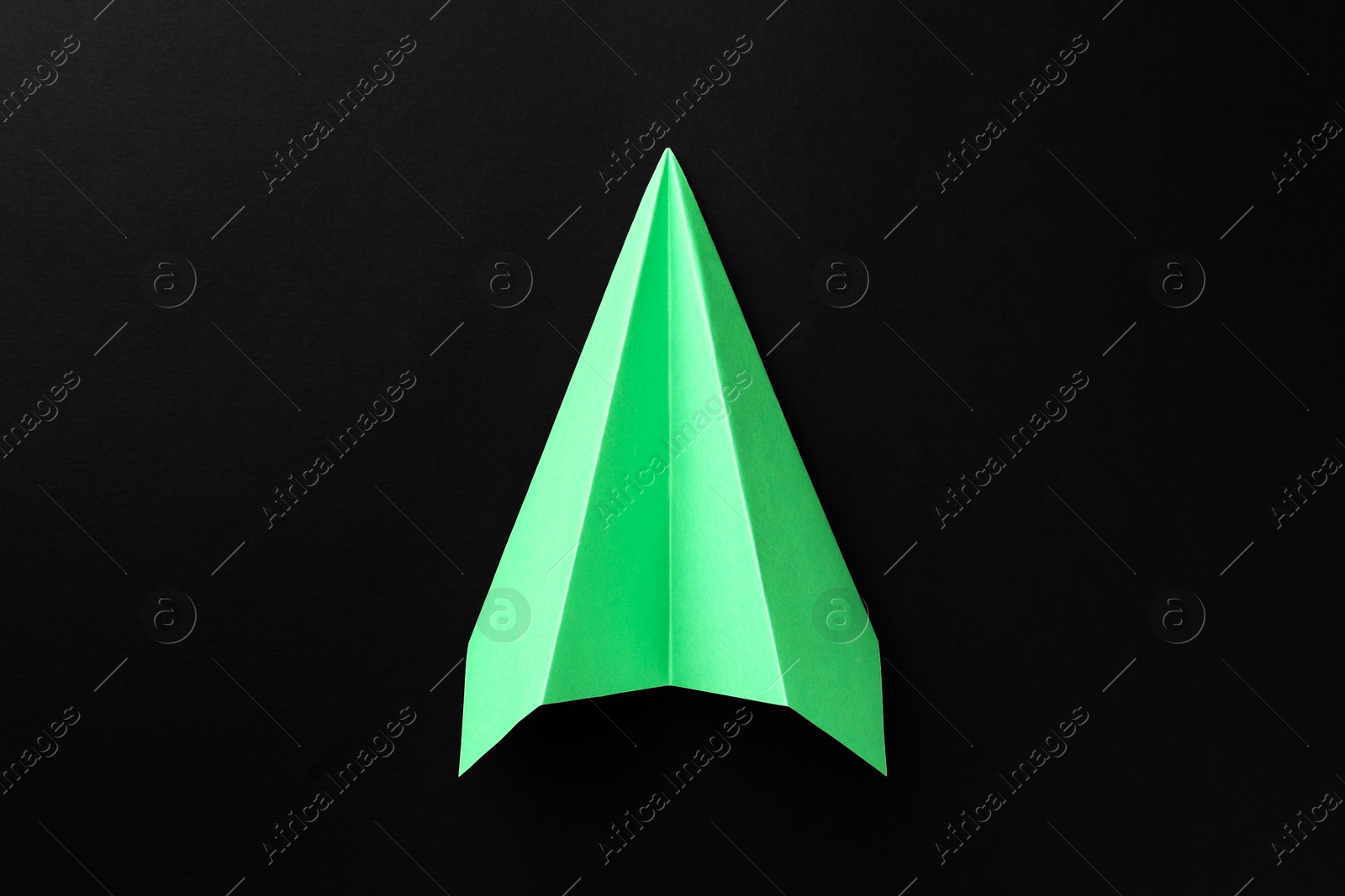 Photo of One handmade green paper plane on black background, top view