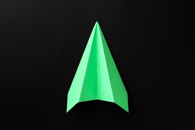 Photo of One handmade green paper plane on black background, top view