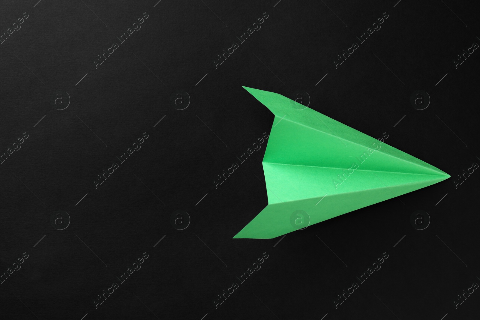 Photo of One handmade green paper plane on black background, top view. Space for text