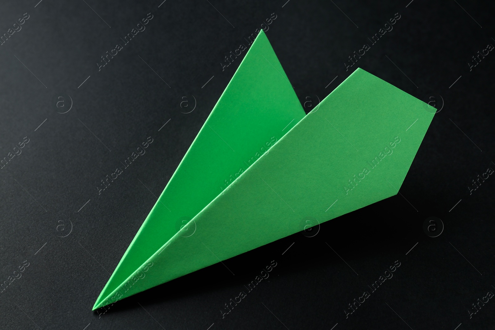 Photo of One handmade green paper plane on black background, closeup