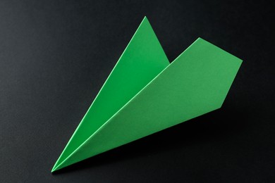 Photo of One handmade green paper plane on black background, closeup