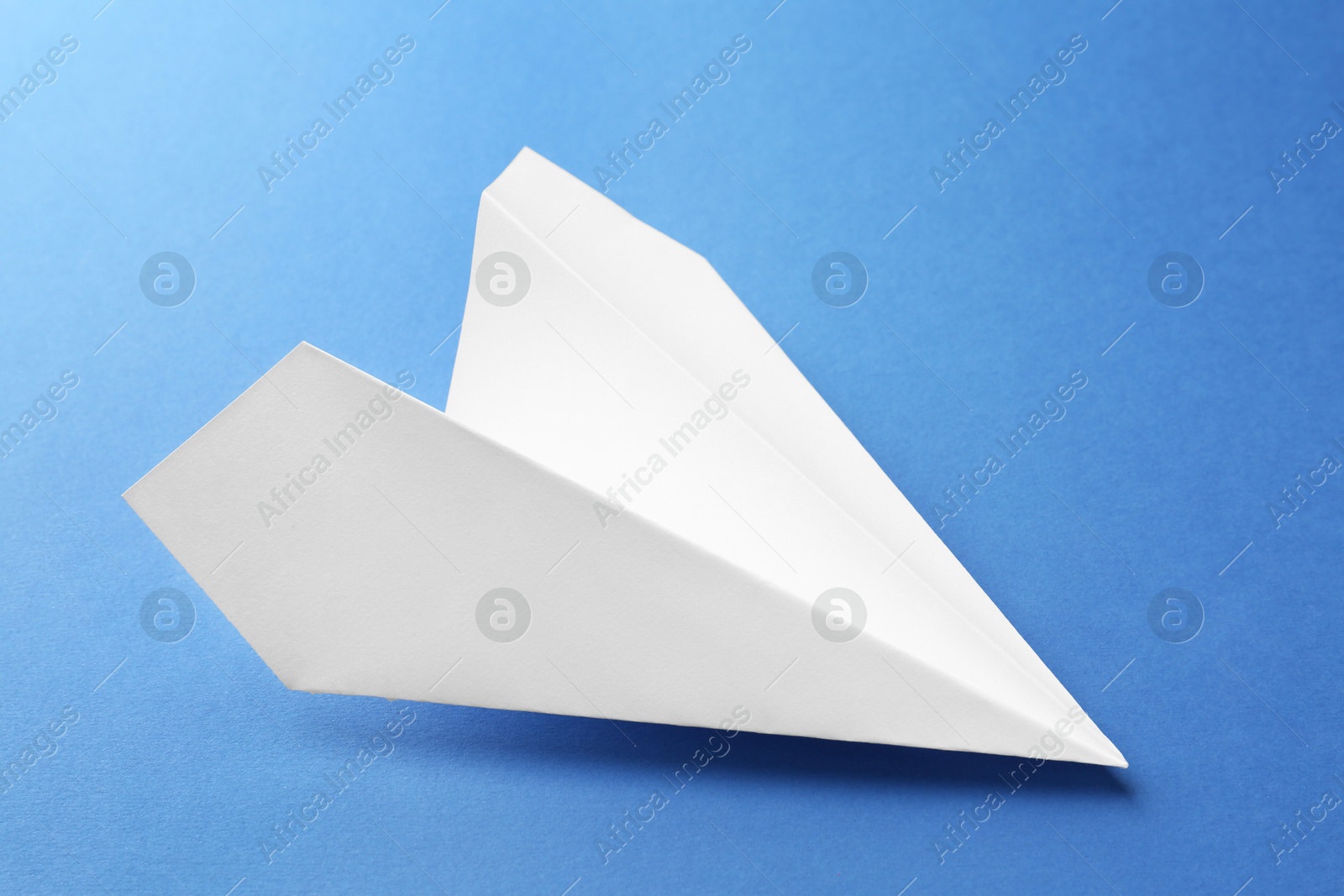 Photo of One handmade paper plane on blue background, closeup