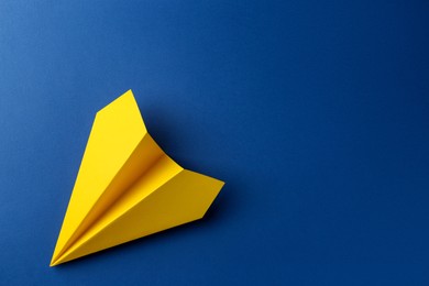 Photo of One handmade yellow paper plane on blue background, top view. Space for text