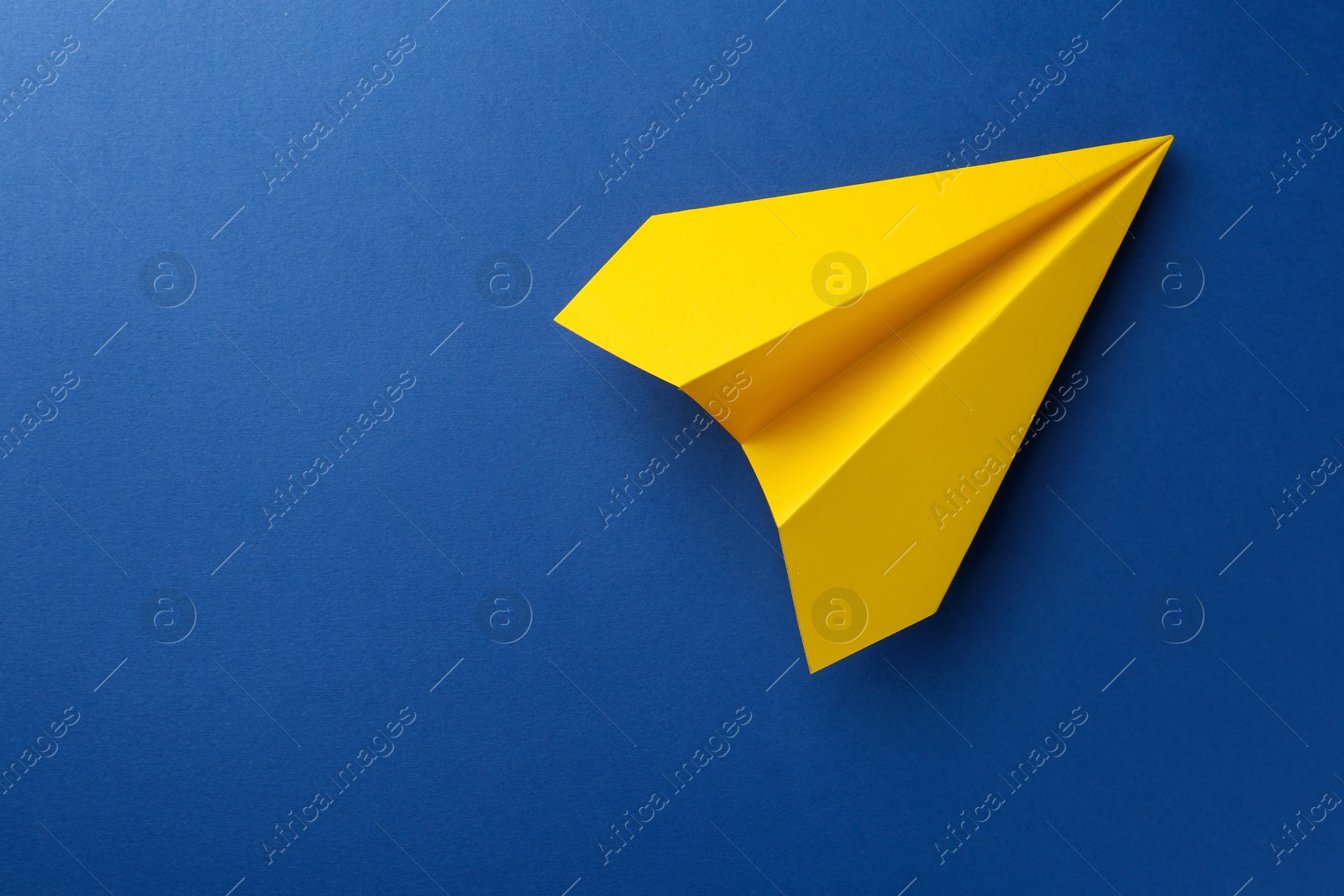 Photo of One handmade yellow paper plane on blue background, top view. Space for text