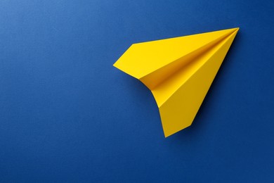 Photo of One handmade yellow paper plane on blue background, top view. Space for text