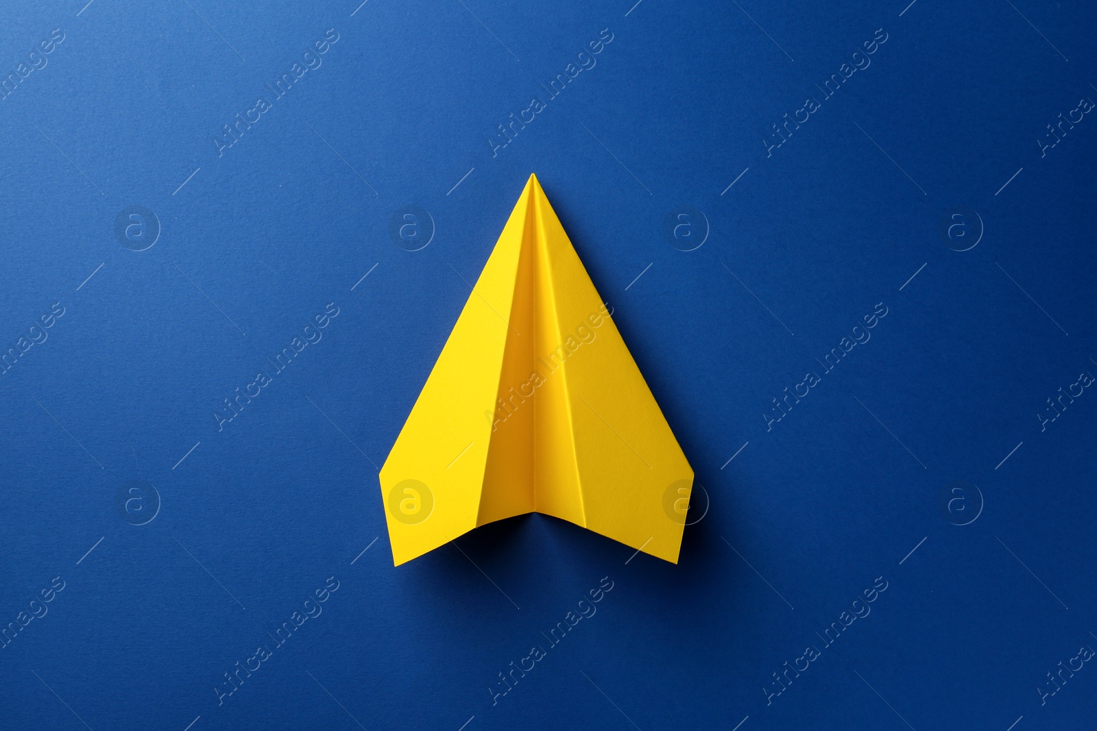 Photo of One handmade yellow paper plane on blue background, top view