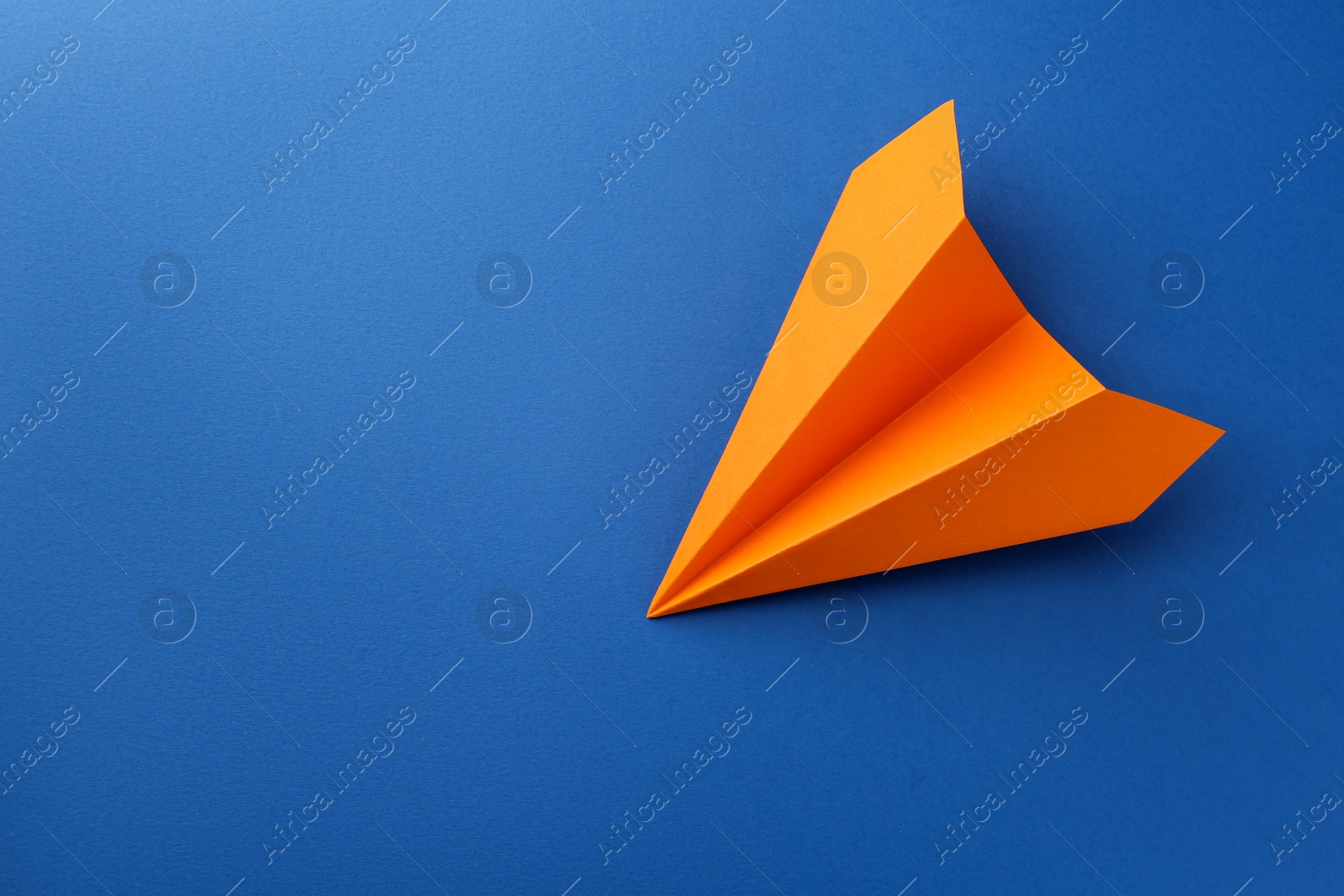 Photo of One handmade orange paper plane on blue background, top view. Space for text