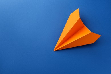 Photo of One handmade orange paper plane on blue background, top view. Space for text