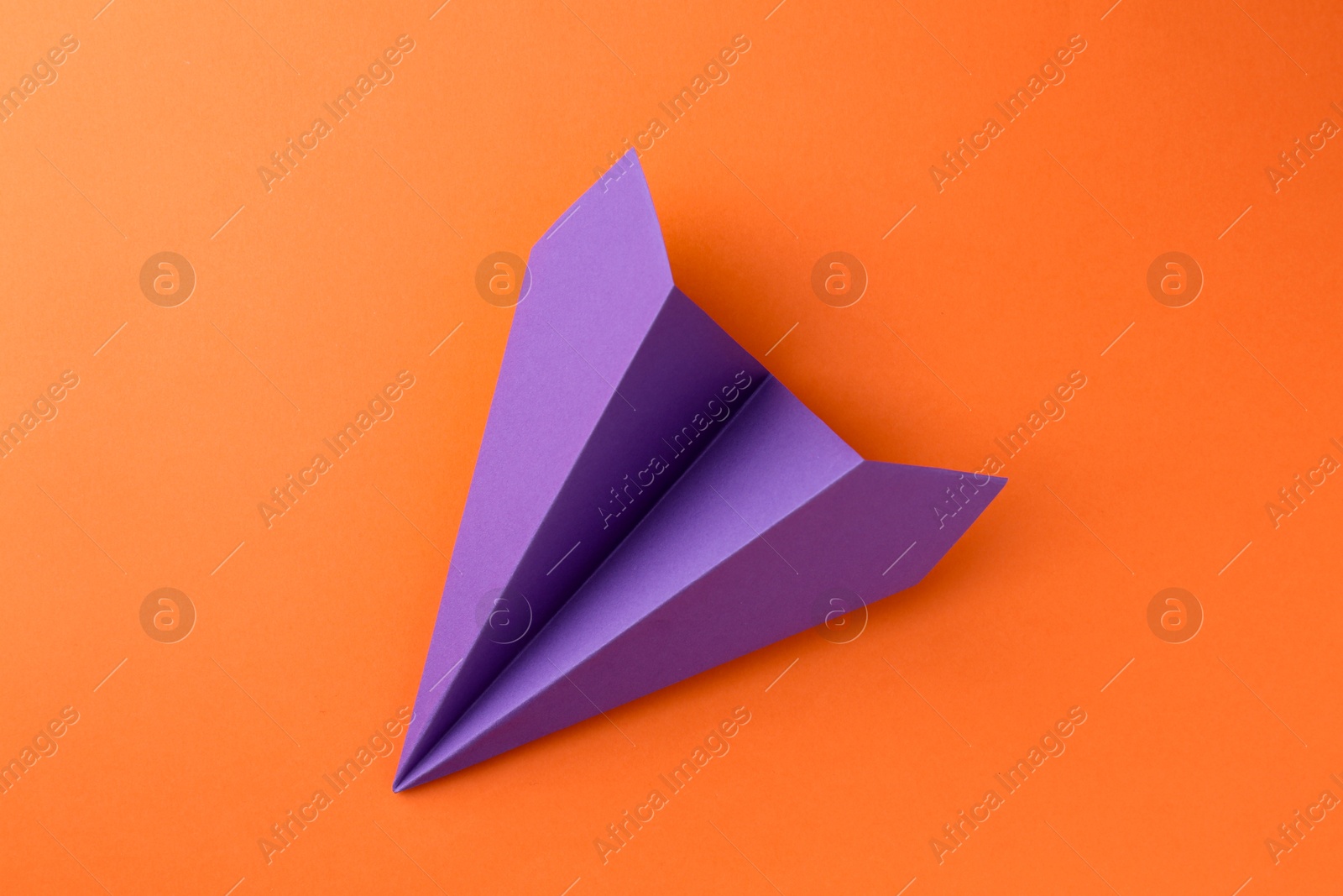 Photo of One handmade violet paper plane on orange background, top view