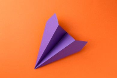 Photo of One handmade violet paper plane on orange background, top view