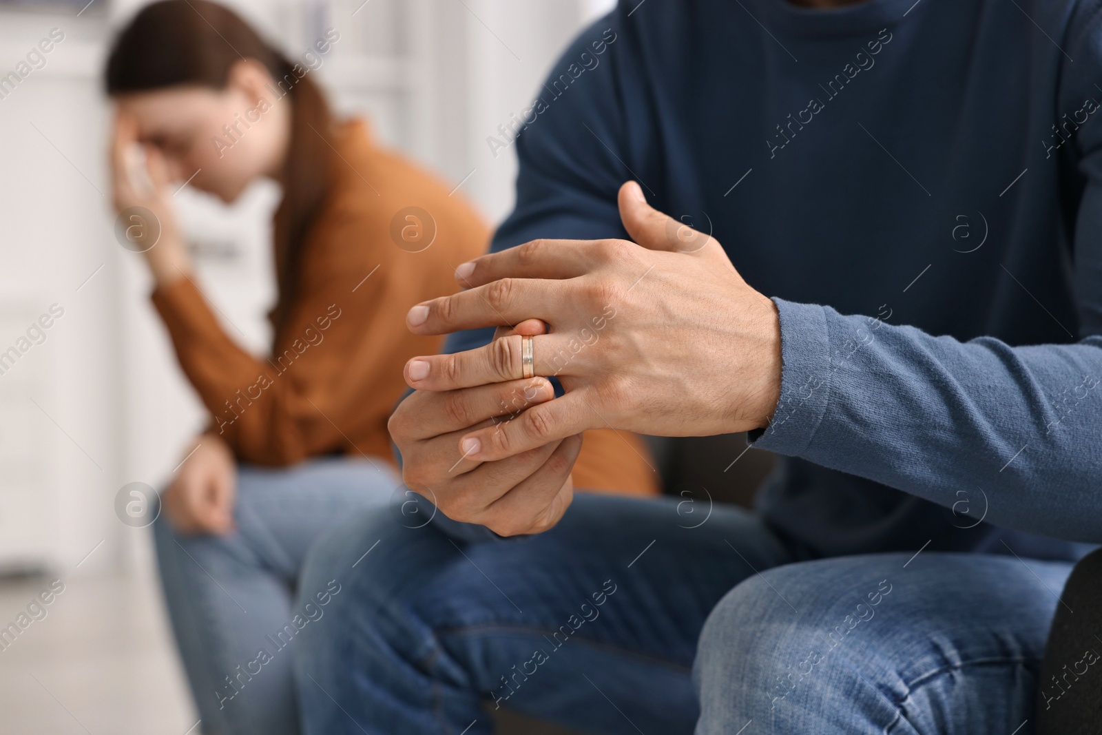 Photo of Man taking off engagement ring after quarrel with his wife at home, closeup