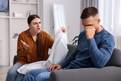 Emotional wife showing shirt with lipstick marks as proof to her unfaithful husband at home