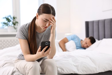 Frustrated woman with husband's smartphone while he sleeping in bedroom, selective focus