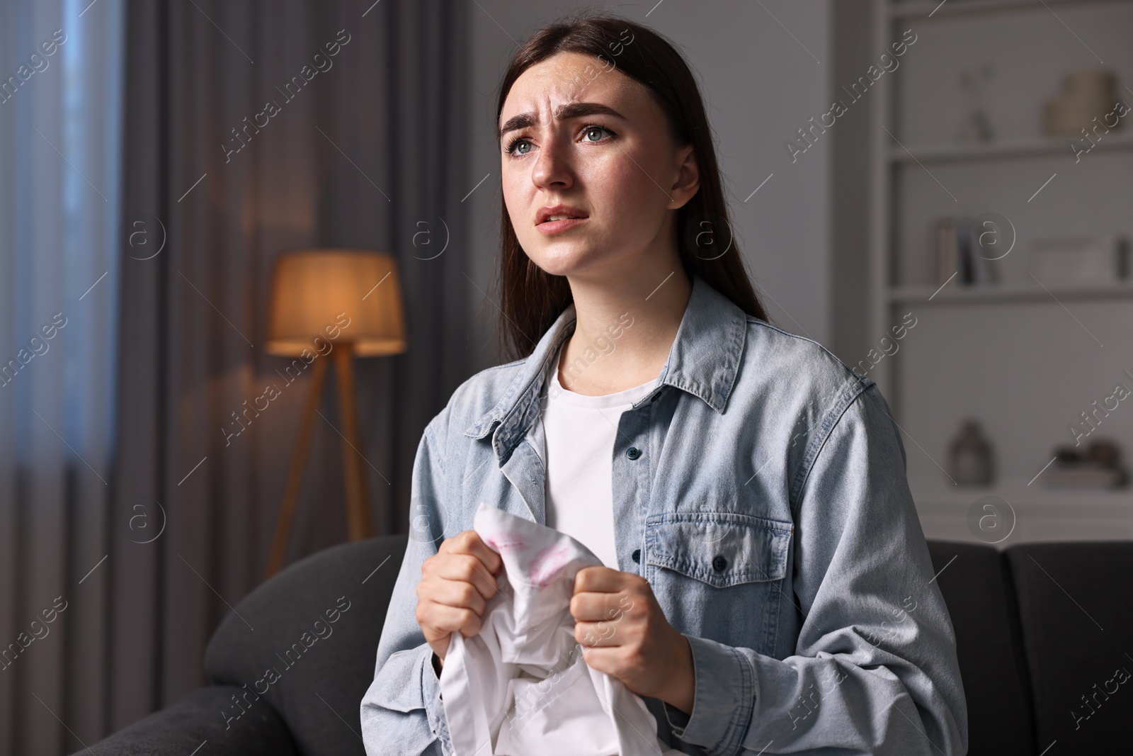 Photo of Frustrated wife holding shirt with lipstick marks as proof of her unfaithful husband at home